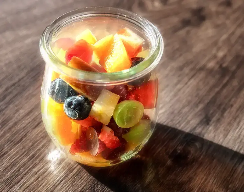 Bicchiere di macedonia di frutta fresca con fragole, ananas, mele e uva.