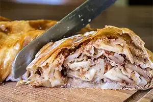 A knife cuts off a piece of apple strudel