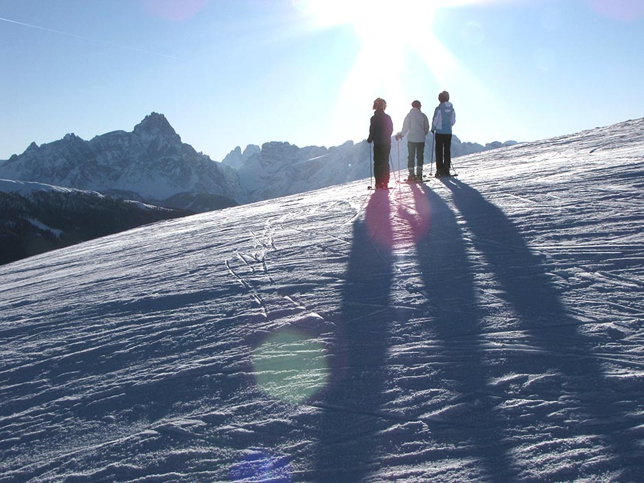 Drei Schifahrer stehen auf der Piste und blicken auf die Sextener Dolomiten.