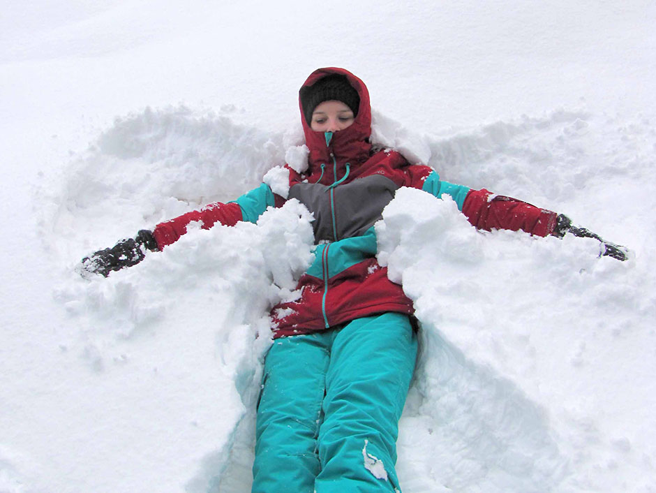 Mädchen liegt im Schnee am Rücken und bildet die Schneefigur "der Engel"