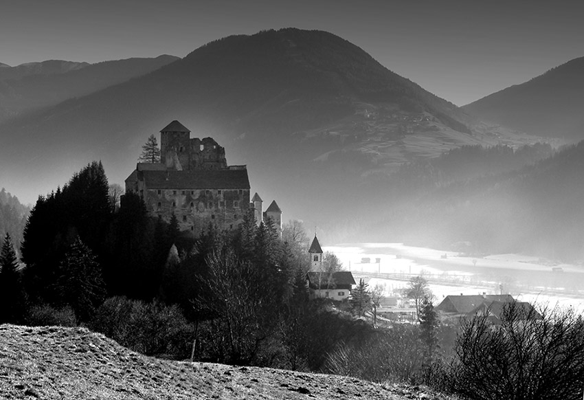 Foto der Burg Heinfels auf dem Burghügel. Im Tal liegt noch Nebel.